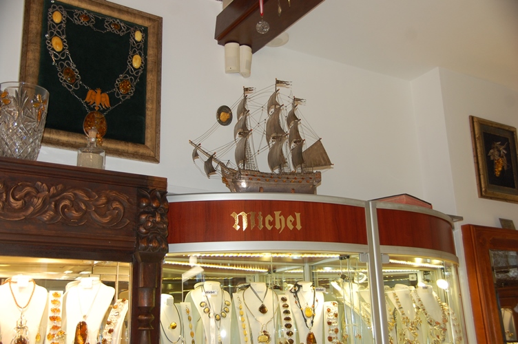 Interior de tienda con objetos en ámbar en vitrinas y expuestas en la pared; destaca la réplica de una barco hecho de ámbar encima de la vitrina y una cadena con insignias en ámbar