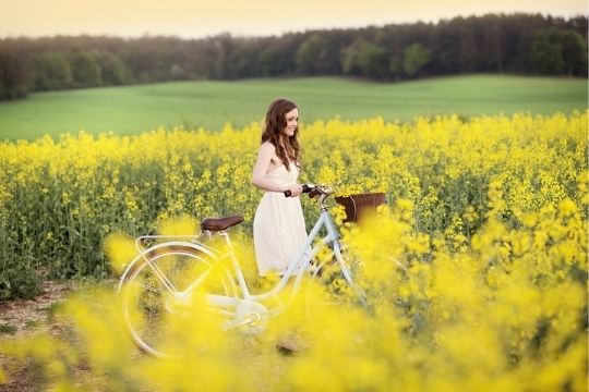 Una ragazza con la bici in una campo di colza fiorita di giallo