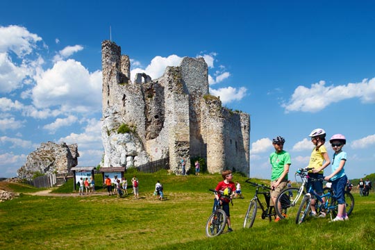 Persone in bicicletta; sullo sfondo, le rovine di un castello