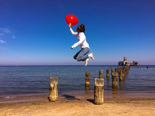 Persona di spalle con in mano un palloncino a forma di cuore su una spiaggia del mar Baltico