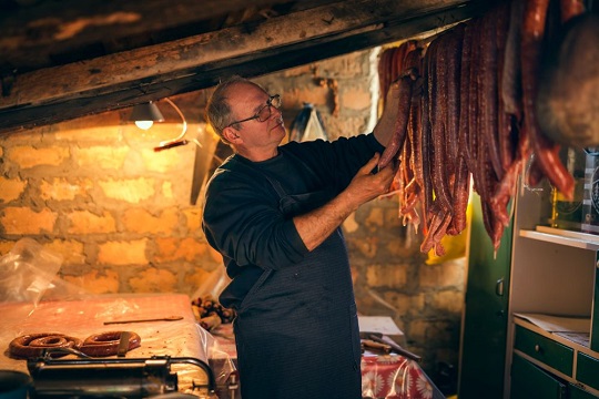Diversas salsichas penduradas em uma loja de artesanato com uma pessoa mostrando o produto