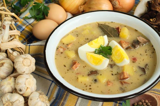 Um prato com sopa bege, com ovos cozidos no meio. Existem especiarias usadas para a preparação, como alho, cebola e louro