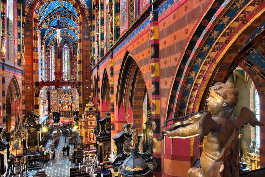 Interior de la Iglesia de Santa María en Cracovia con vista, en el fondo, al altar de madera; ricas ornamentaciones de las paredes de colores vivo; la figura de un ángel tocando violín en primer plano