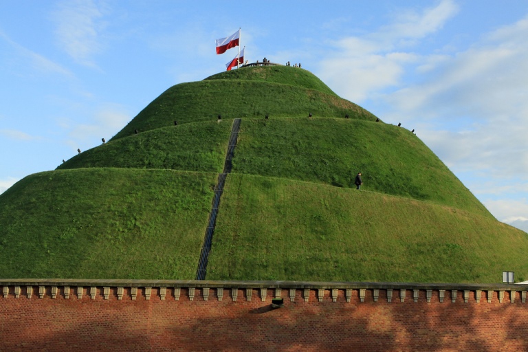 Un montículo bastante alto, cubierto de césped; se ve el sendero serpenteando que lleva a la cima, decorada con la bandera de Polonia, en blanco y rojo