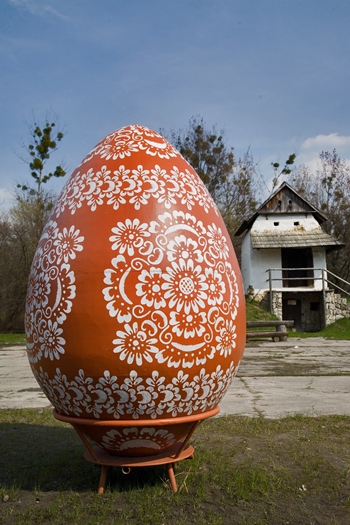 Huevo de Pascua pintado a mano, de grandes dimensiones, expuesto delante de una edificación de madera