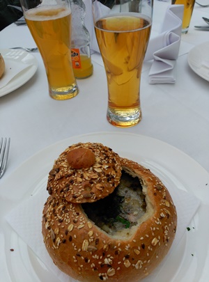 en primer plano, una hogaza de pan que sirve de plato para servir una sopa, vasos altos de cristal con cerveza