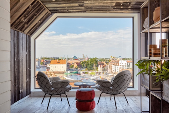 cómodos y modernos sillones delante de una pared de cristal con vistas al casco antiguo de Gdansk; hotel PURO Gdansk