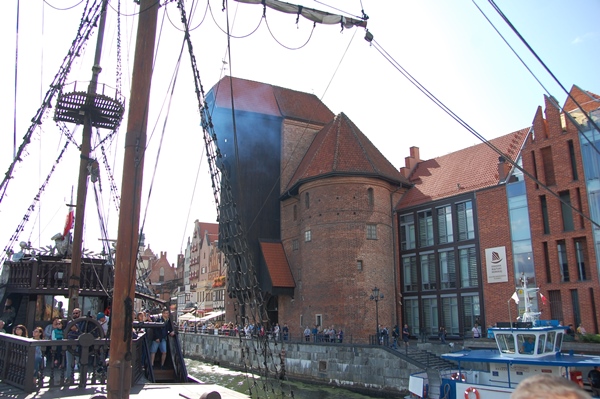 entre los mástiles de un barco histórico se  ve la construcción de ladrillo, de considerable altura, situado en la proximidad del muelle