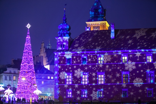 Fachada del castillo en la cual se proyectan motivos navideños, árbol de Navidad y panorama de edificios históricos altos en el fondo, 
