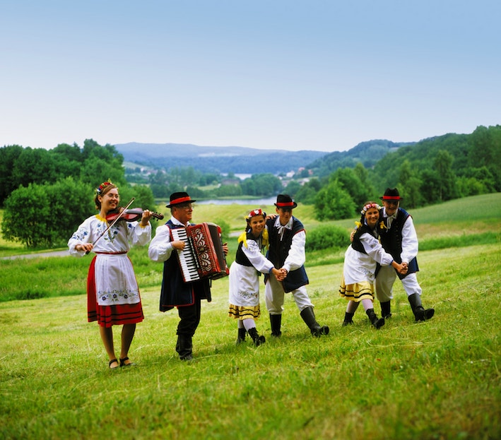 6 persone vestite con abiti folcloristici della Casciubia che suonano e ballano in mezzo al prato verde