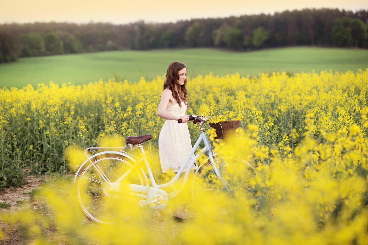 Ragazza sorridente con una bici accanto in un campo di fiori gialli