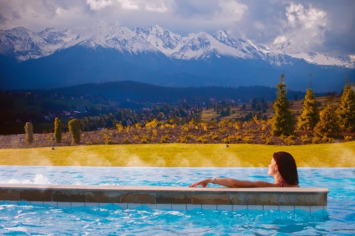 Foto di una ragazza mentre si rilassa in una piscina all'aperto, belle terme Bania. Sullo sfondo, delle montagne innevate