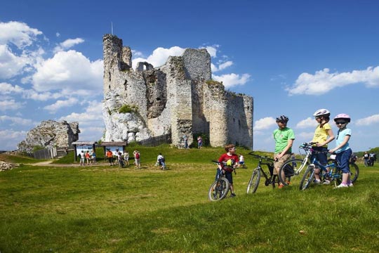 Sullo sfondo, le rovine di un castello. In primo piano, delle persone in bici