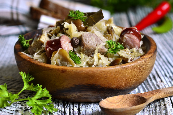 Immagine di bigos myśliwski- pietanza polacca a base di crauti cotti e carne, funghi e prugne secche. Servito in una ciotolina di legno.