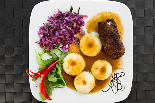 Foto di un piatto contenente gli gnocchi di patate tipici della Bassa Slesia con un'involtino di carne accompagnati dall'insalata di verza rossa.