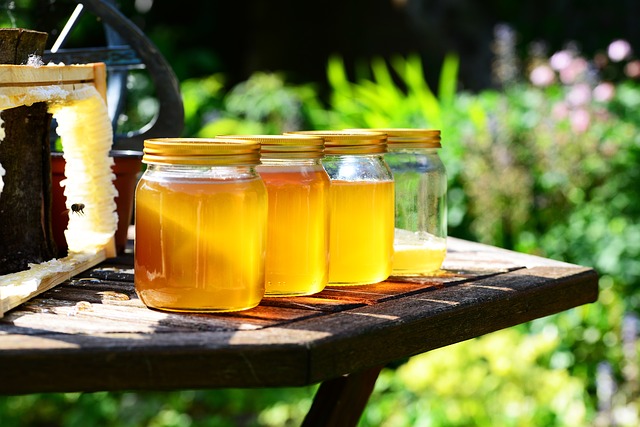 Quattro barattoli di miele, di cui solo tre sono pieni. Appoggiati su un tavolo di legno in un giardino. 