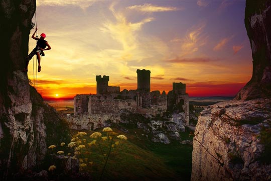 Persona che pratica arrampicata; sullo sfondo, le rovine di un castello al tramonto